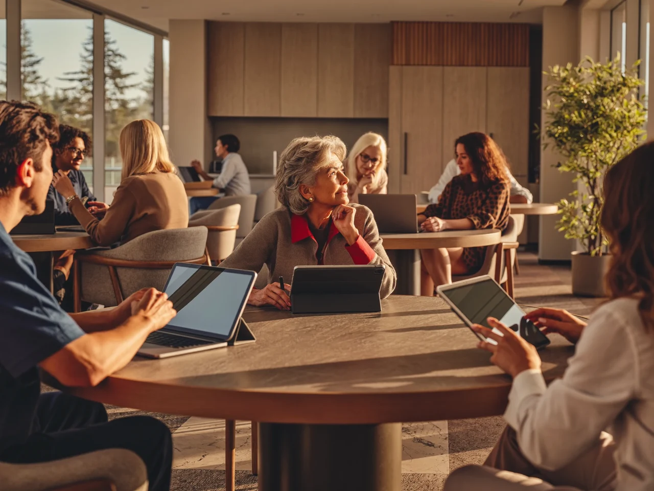 Sala luminosa con persone anziane e giovani tutor al lavoro su tablet e portatili