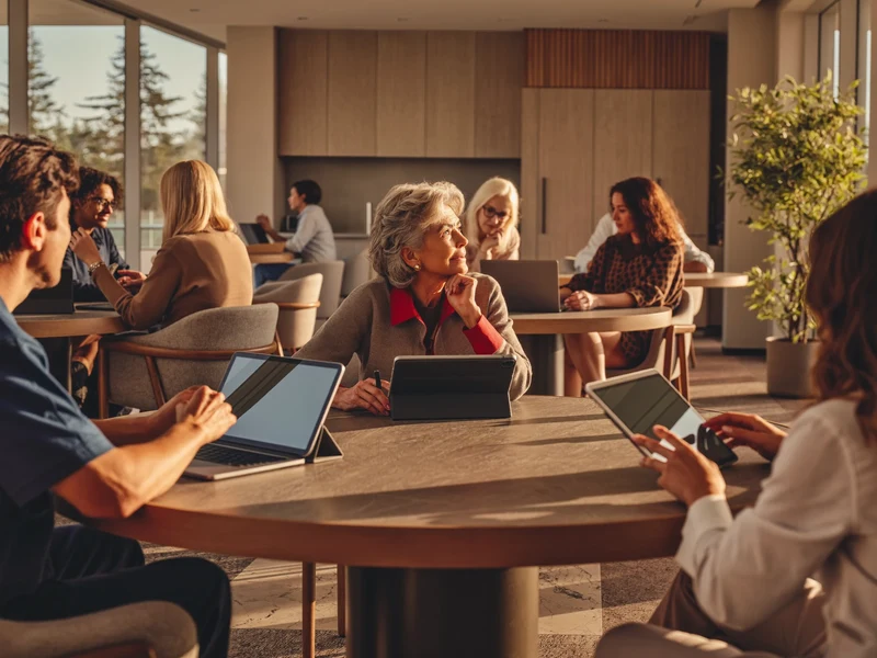 Sala luminosa con persone anziane e giovani tutor al lavoro su tablet e portatili