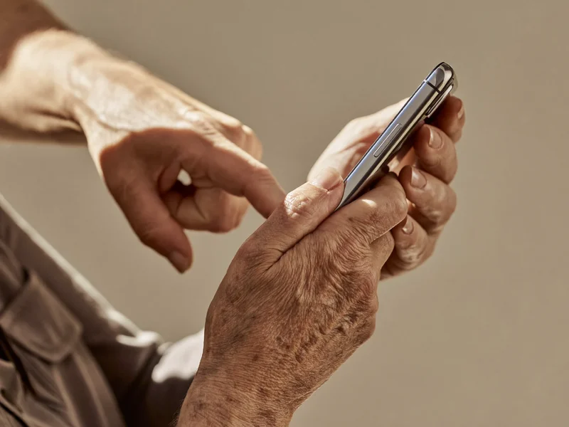 Primo piano di mani anziane che tengono uno smartphone, pronte a toccare lo schermo